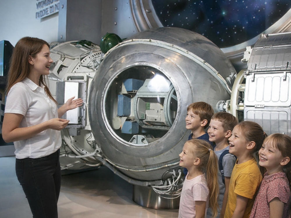 Дети с гидом на экскурсии у элемента космического корабля